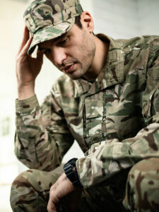 Image of a serviceman with PTSD holding his head in one hand and looking down. Wounded Veteran Fund