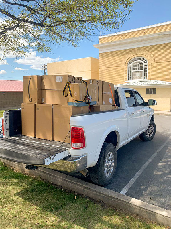 Image of a white pickup truck with the tailgate down and the bed full of large boxes containing suitcases that CharityRx donates.