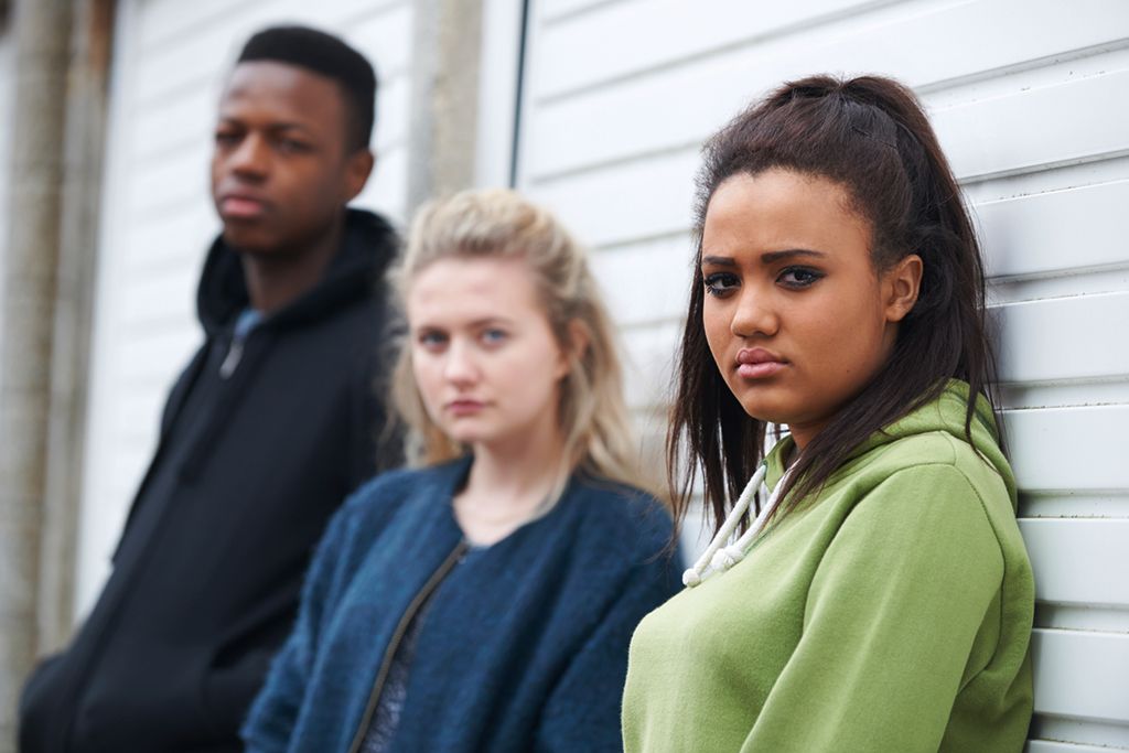 Three sad looking teenage runaways lean against a building.