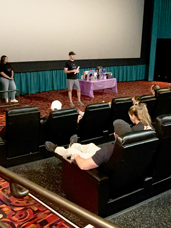 At the front of a movie theater, CharityRx founder speaks to the military families at the Operation Give Hope movie event.