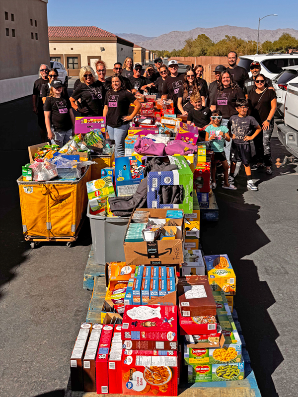 Behind a long line of dollies filled with donated food and clothing, a large group of CharityRx team members pose together.