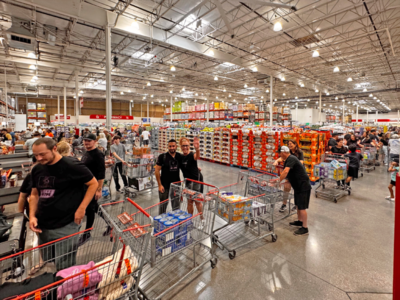 A group of CharityRx team members in a very long checkout line, purchasing food donations for Project 150. A man and woman lean together in the center of the photo, smiling and waving.