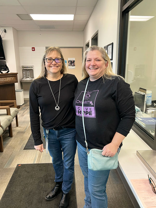 Two middle-aged women stand next to each other smiling.