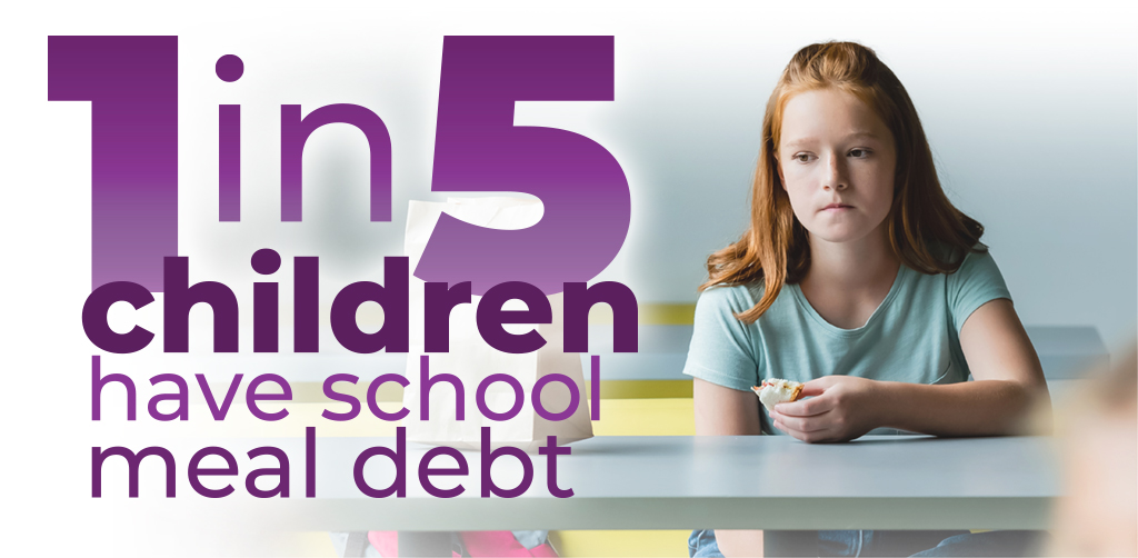 1 in 5 children have school meal debt. A sad young girl sits at a lunch table holding a partially eaten peanut butter sandwich.